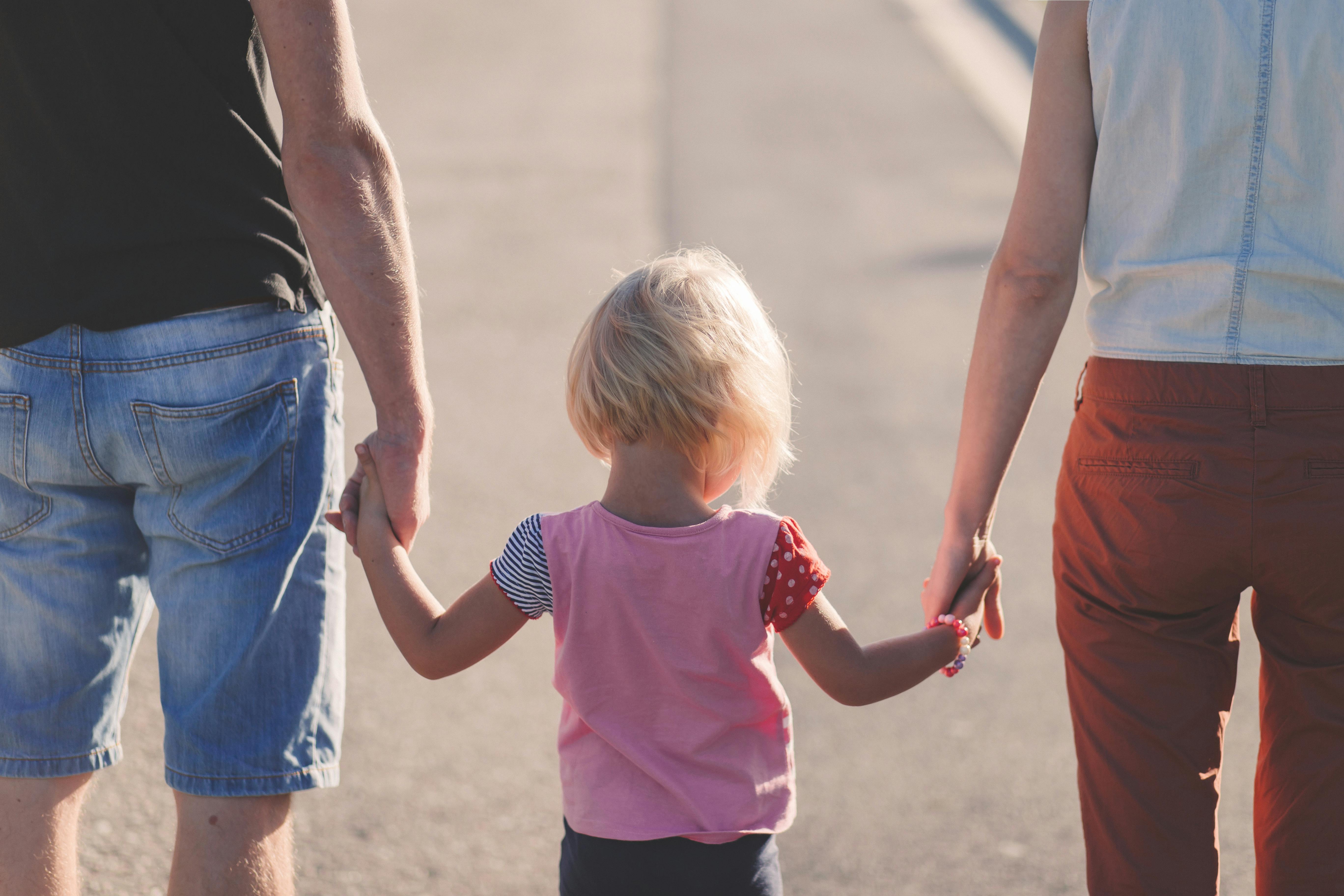 Child holding hands with two adults while walking together